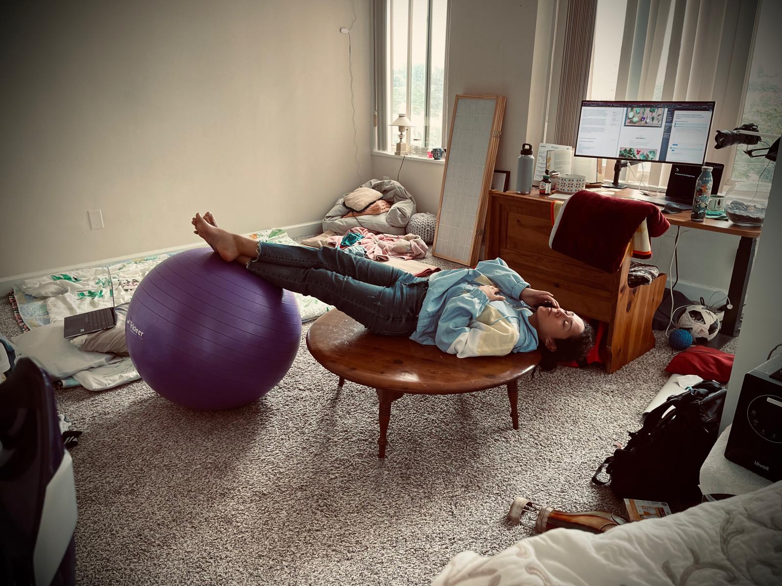Aries relaxing playfully on a round coffee table in their creative workspace, with legs propped up on an exercise ball
